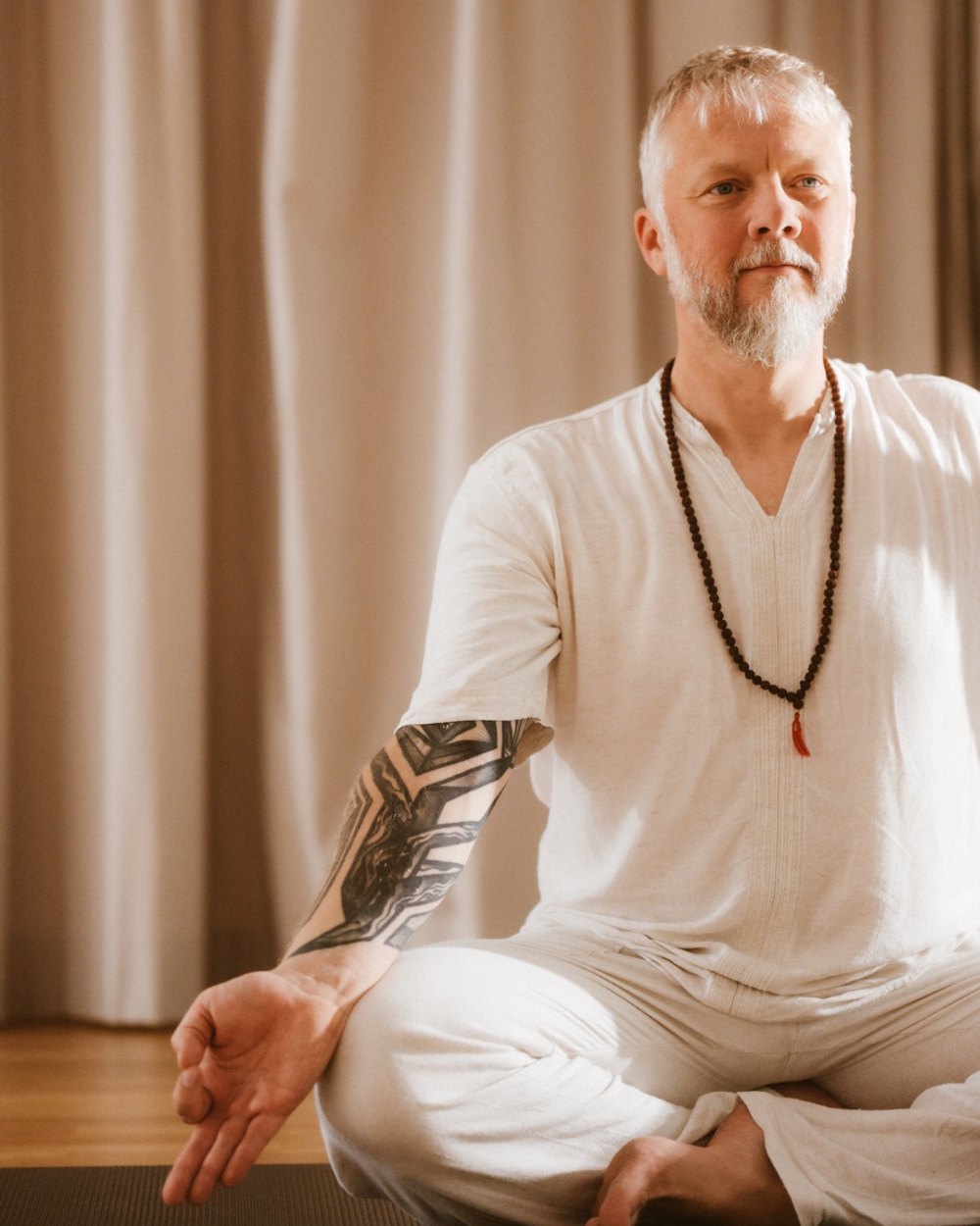 Sebastian Braun im Schneidersitz in weisser Kleidung mit Mala
